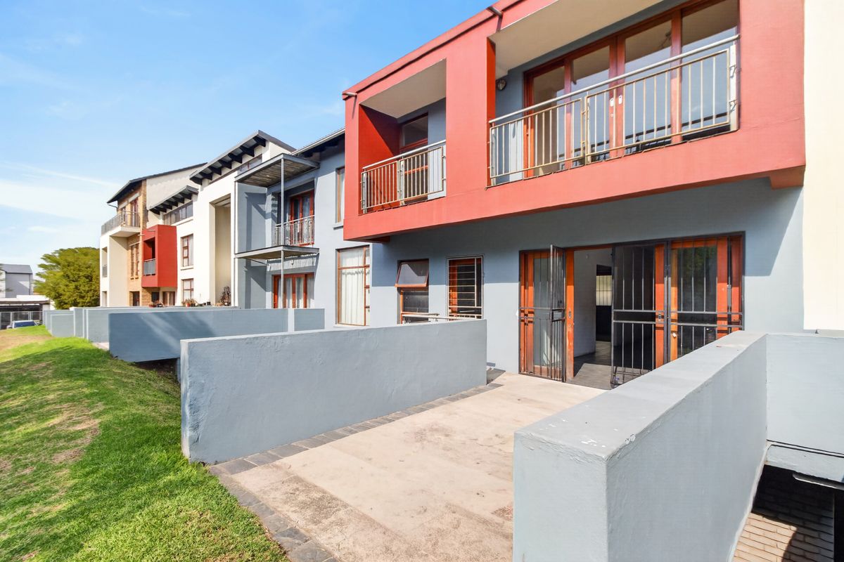 Rear view of a modern apartment complex featuring ground floor concrete patios, upper-level balconies with metal railings, and secure access points.