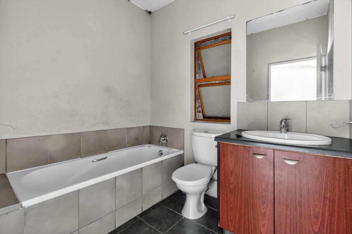 A dated bathroom featuring a bathtub, toilet, and vanity basin. The space requires cosmetic updates to the walls and window frame.