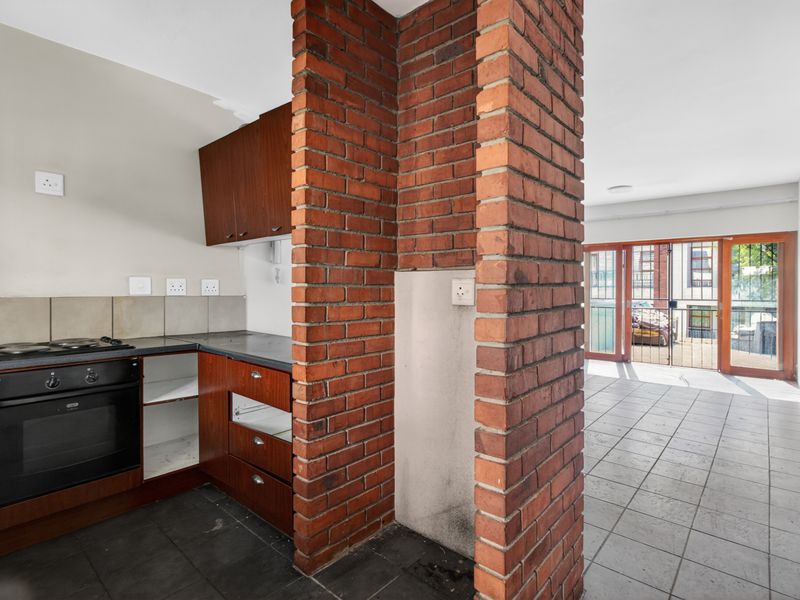 Open plan kitchen and living area featuring an exposed brick pillar, tiled flooring, and direct access to an outdoor patio through sliding glass doors.