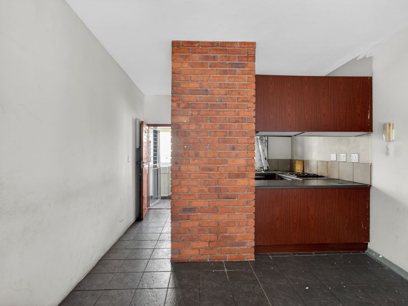 Open plan kitchen area featuring a distinctive exposed brick pillar, dark wood cabinetry, and tiled flooring, leading to an exterior security gate.