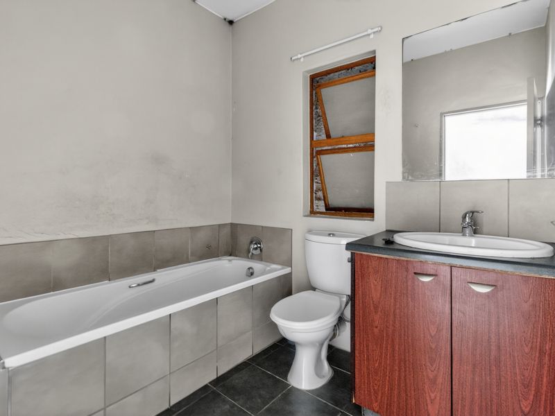 A dated bathroom featuring a bathtub, toilet, and vanity basin. The space requires cosmetic updates to the walls and window frame.