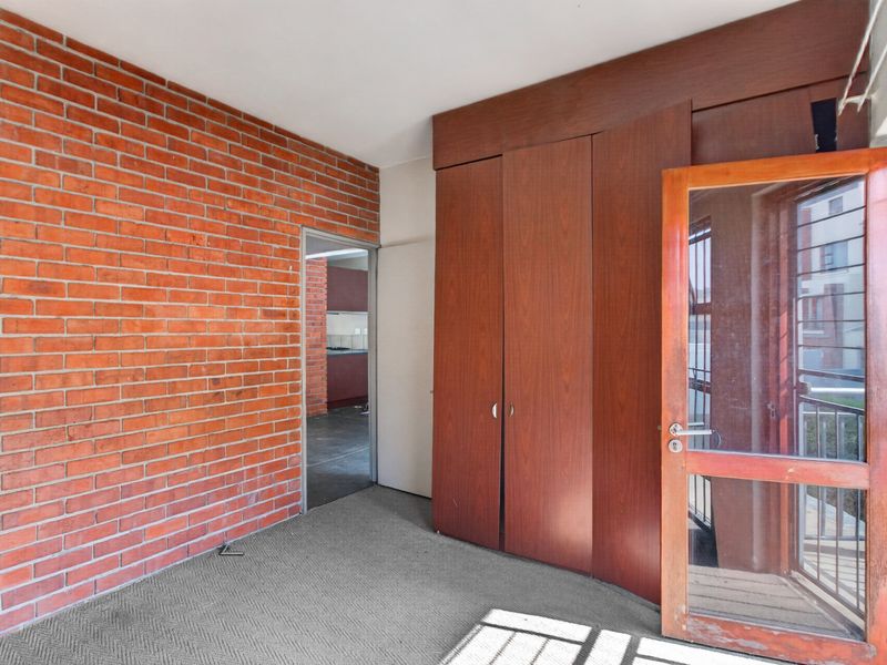 A bedroom featuring an exposed brick wall, built-in wooden cupboards, and a glass panel door leading to an outdoor area.