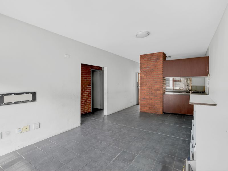 Open-plan living and kitchen area featuring tiled floors, an exposed brick feature pillar, and built-in cabinetry.