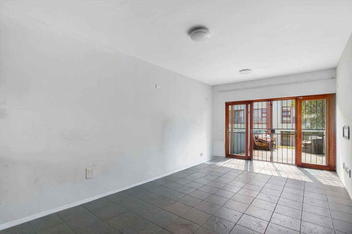 An empty living room featuring tiled flooring and a sliding glass door with a security gate leading to an outdoor area.