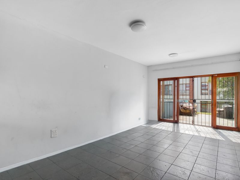 An empty living room featuring tiled flooring and a sliding glass door with a security gate leading to an outdoor area.