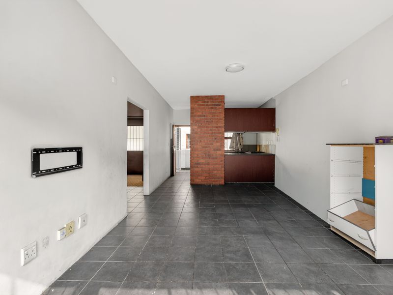 An open-plan living and kitchen area featuring dark tiled flooring, an exposed brick feature column, and built-in kitchen cabinetry.