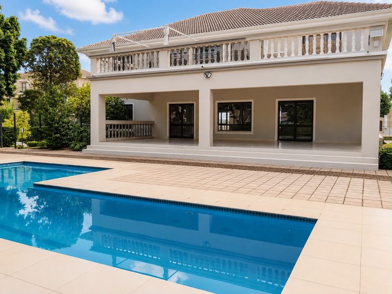 A well-maintained outdoor area featuring a clear swimming pool, tiled pool deck, and a spacious covered patio with a classic balustrade.