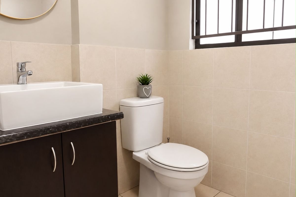 A clean and modern bathroom featuring a vessel sink on a dark vanity cabinet, a white toilet, and neutral wall tiling.