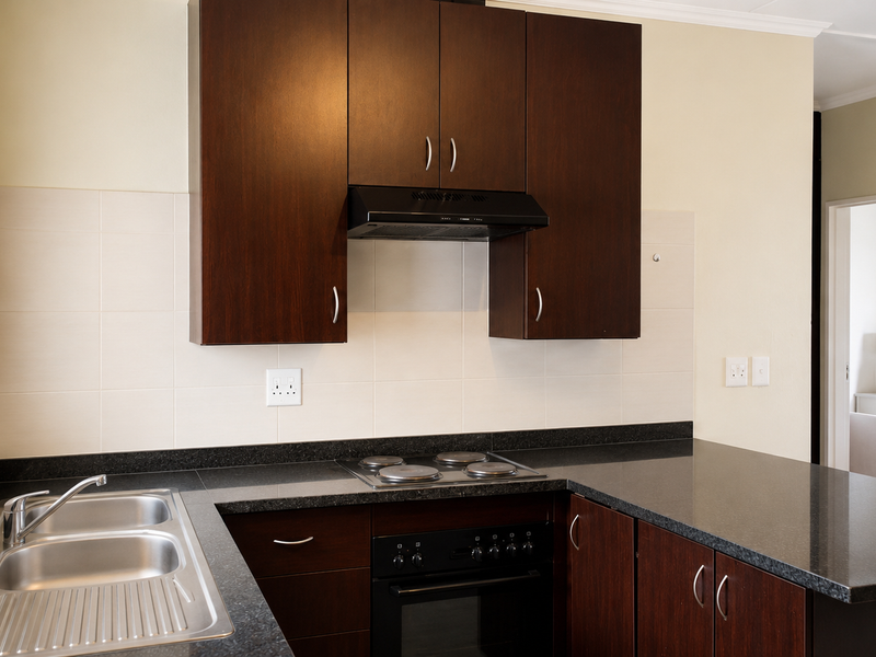 A functional kitchen featuring dark wood cabinetry, black granite countertops, a built-in oven, electric hob, and a stainless steel double sink.