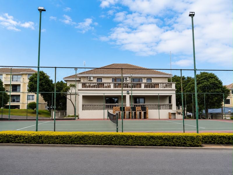 A well-maintained tennis court facility located within the apartment complex grounds, featuring perimeter fencing and floodlighting.