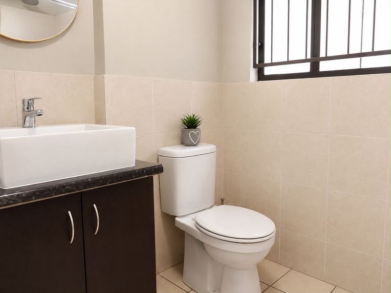 A clean and modern bathroom featuring a vessel sink on a dark vanity cabinet, a white toilet, and neutral wall tiling.