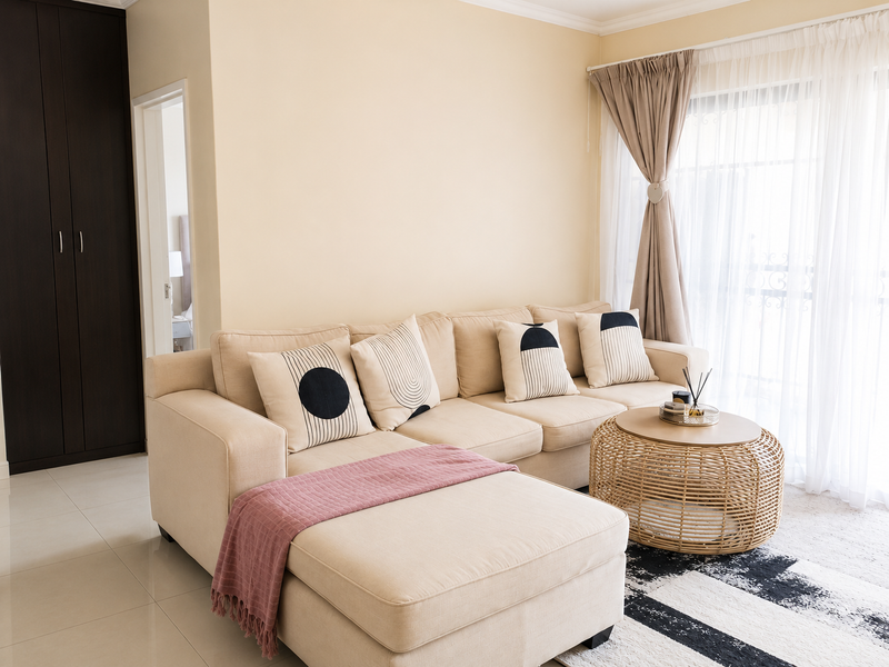 A bright and well-maintained living room featuring neutral tiled flooring, a dark built-in cupboard, and access to a balcony through sliding glass doors.