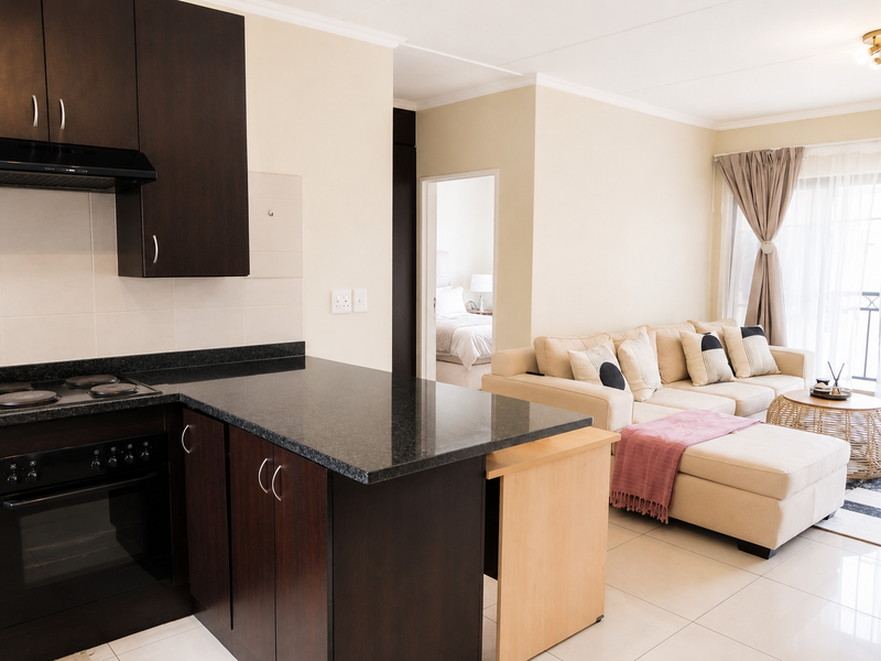 Modern open-plan apartment featuring a sleek kitchen with dark cabinetry and granite countertops, flowing seamlessly into a bright, tiled living area.