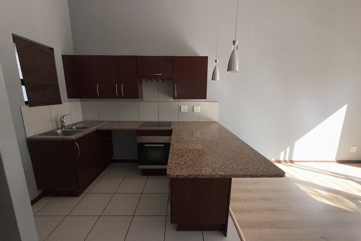 A functional kitchen featuring dark wood cabinetry, granite countertops, a built-in oven and hob, and tiled flooring with an integrated breakfast bar.