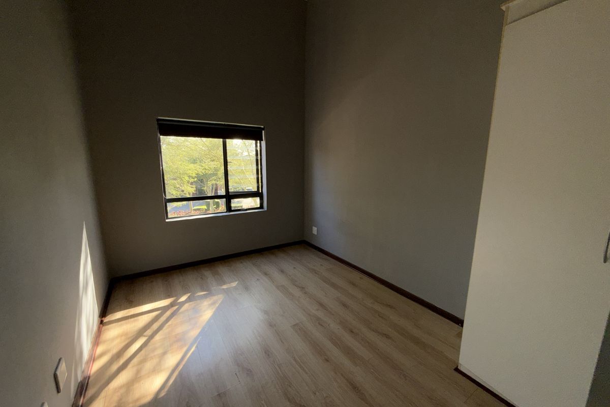 A bright, empty bedroom featuring laminate flooring, neutral grey walls, and a built-in cupboard, offering a clean canvas for personalization.