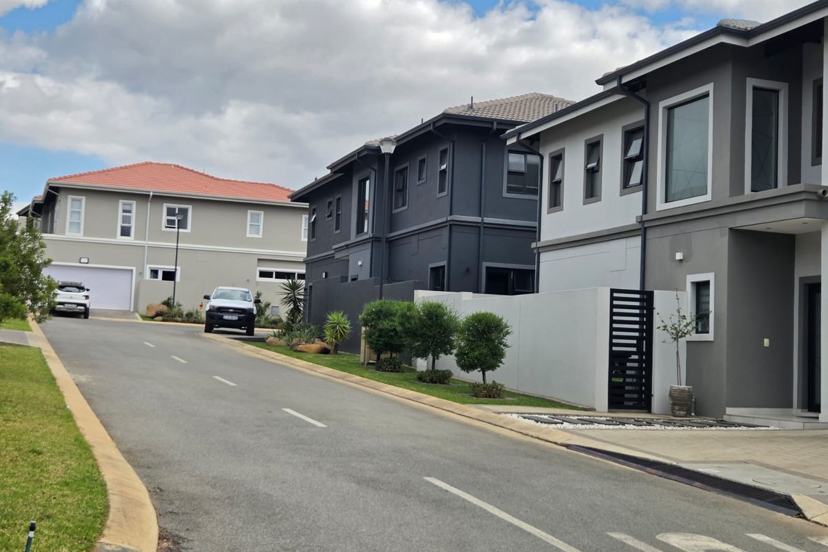 A street view of a modern residential complex featuring contemporary multi-story apartment buildings with paved driveways and secure boundary walls.