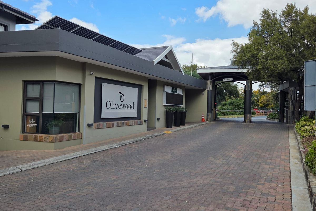 The entrance to Olivewood Estate featuring a paved driveway, security gate, and modern building facade with solar panels.