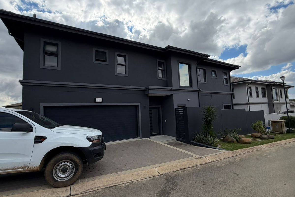 Modern double-story apartment exterior featuring a dark charcoal facade, integrated double garage, and paved driveway entrance.