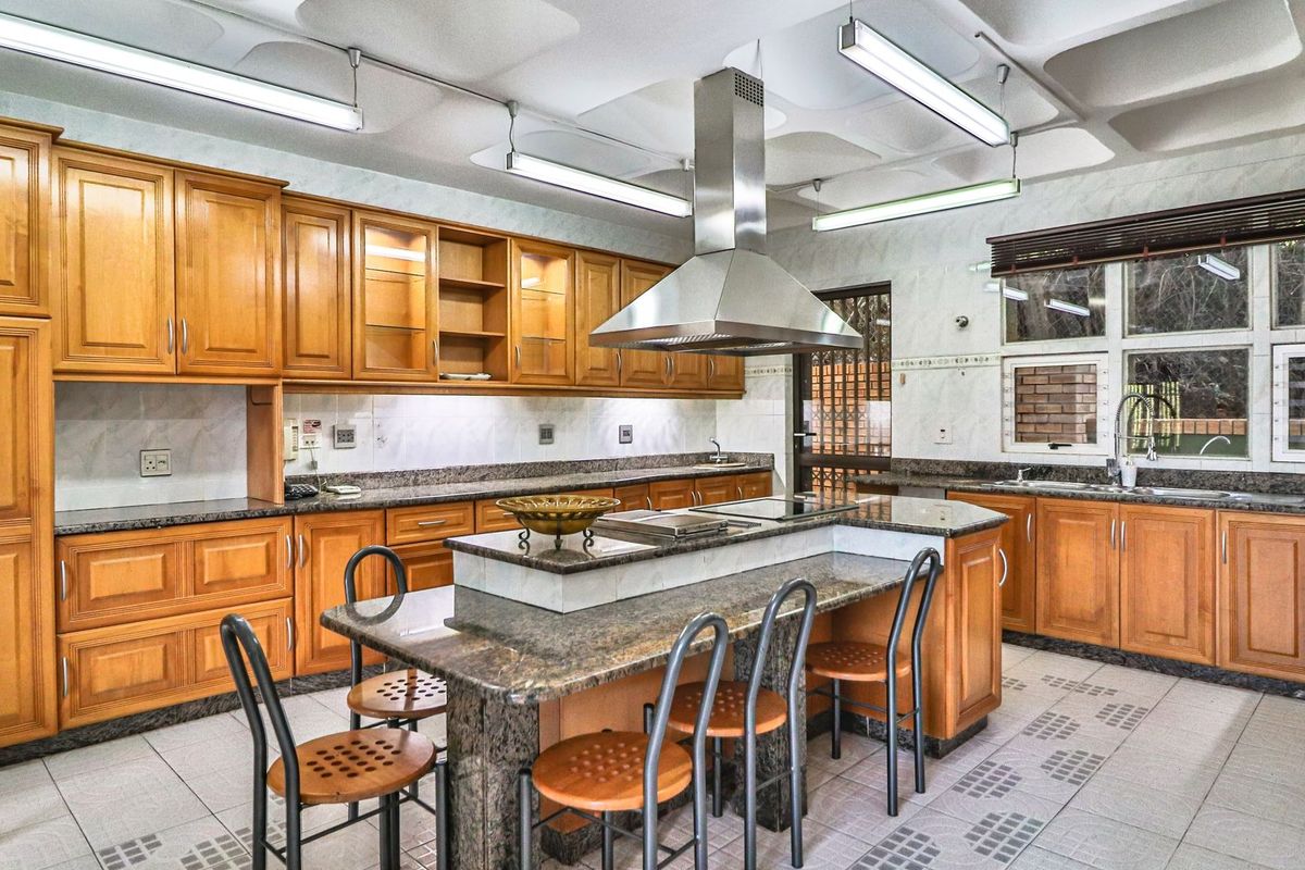 Spacious kitchen featuring extensive wooden cabinetry, granite countertops, a central island with built-in hob, and a distinctive coffered ceiling with integrated lighting.