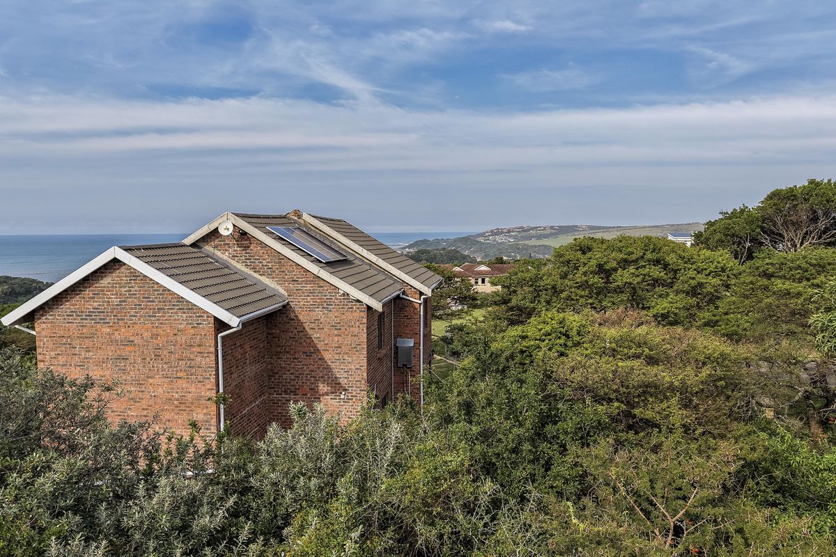 Rear view of a brick residential property featuring a tiled roof with integrated solar panels, set amidst lush greenery with a distant ocean view.