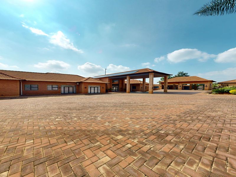 Spacious front exterior featuring a large brick-paved driveway, a covered entrance portico, and a well-maintained face brick facade with a tiled roof.