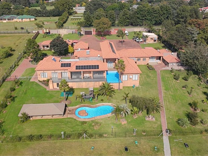 Aerial view of a large residential property featuring a spacious landscaped garden, swimming pool, solar panels, and extensive paved driveway areas.