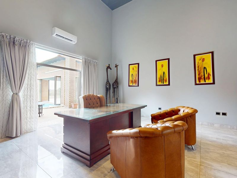 A bright home office featuring high ceilings, tiled flooring, and a large sliding glass door providing direct access to the outdoor patio area.