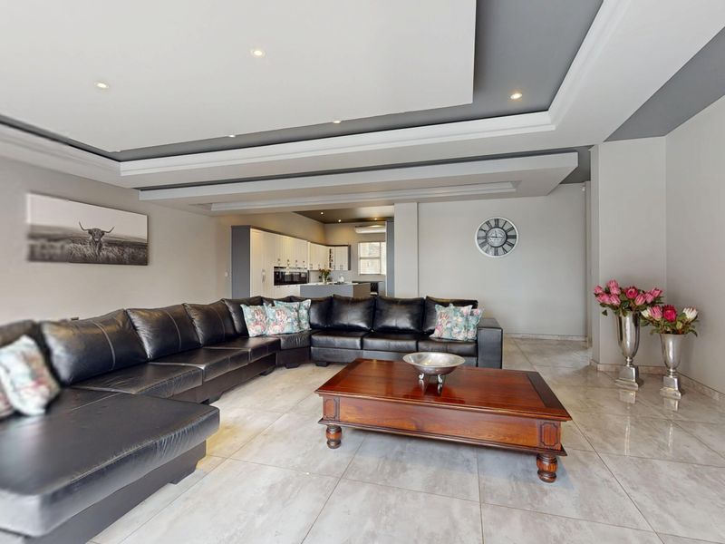Spacious open-plan living area featuring modern tiled flooring, a sophisticated recessed ceiling with downlights, and a seamless transition to the kitchen.