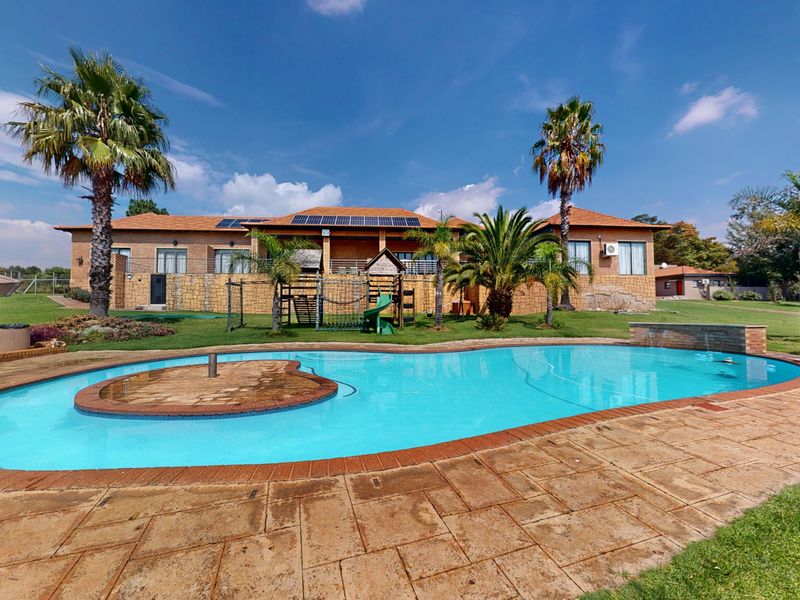 Spacious backyard featuring a large swimming pool with a central island, paved patio area, and a well-maintained garden with solar panels on the roof.