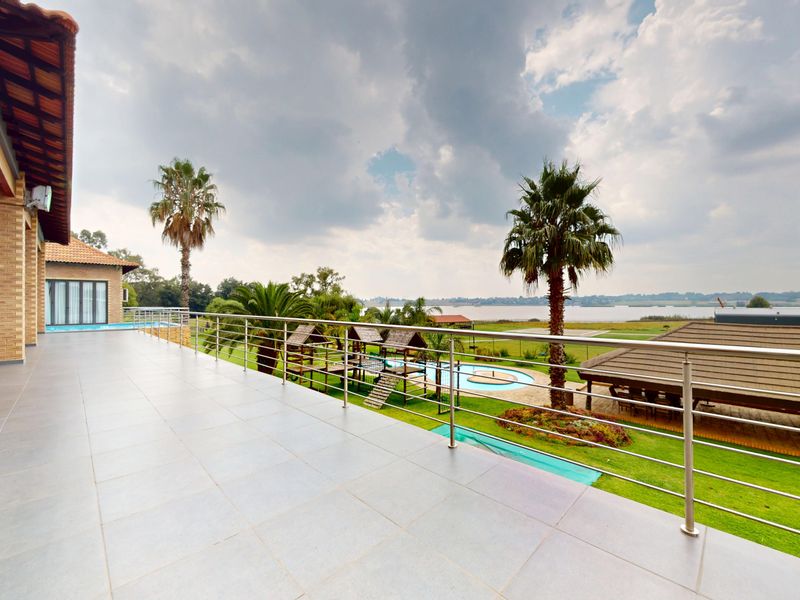 Spacious covered patio featuring tiled flooring and a stainless steel balustrade, offering expansive views of the garden, pool area, and surrounding landscape.