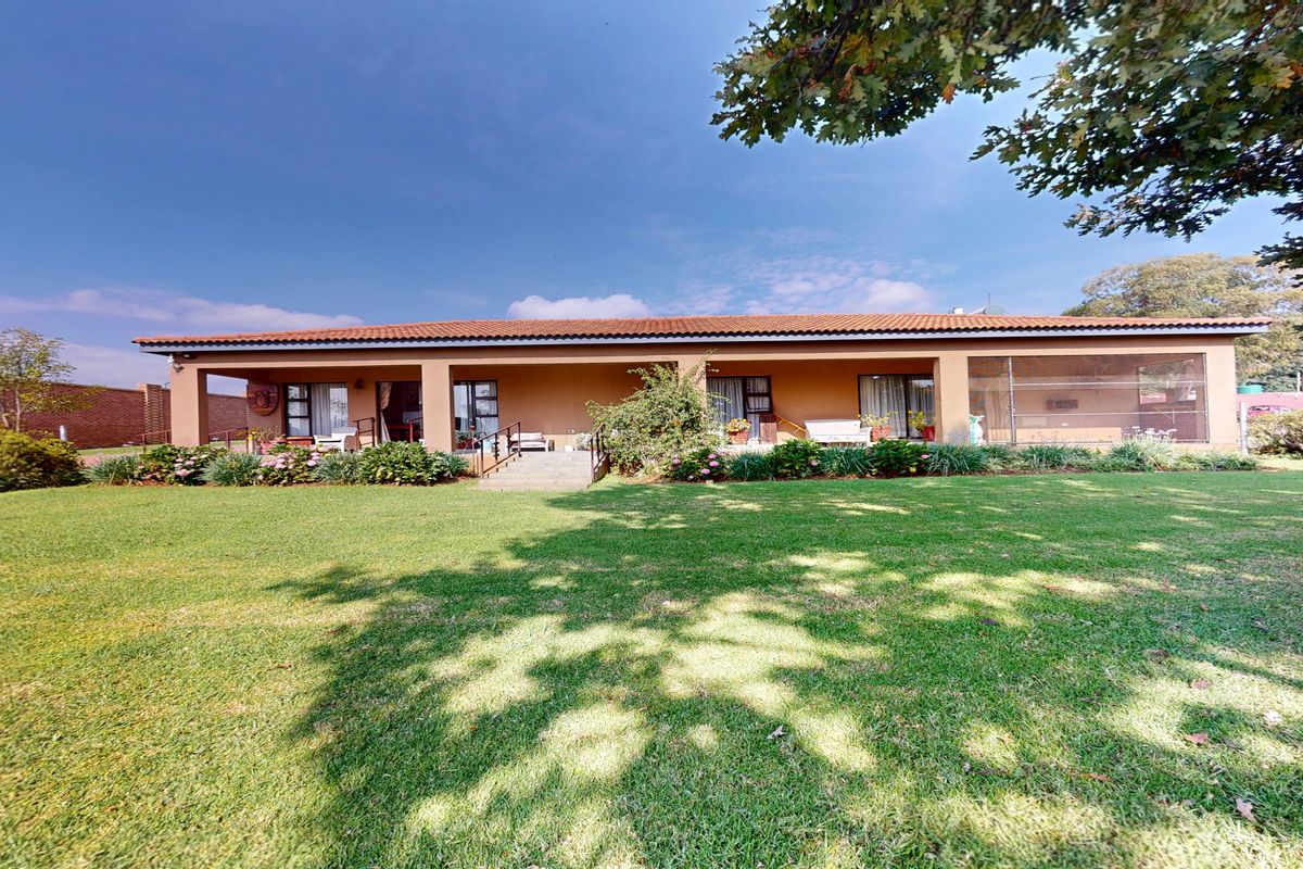 A spacious rear view of the house featuring a large manicured lawn, a covered patio area, and a tiled roof structure.