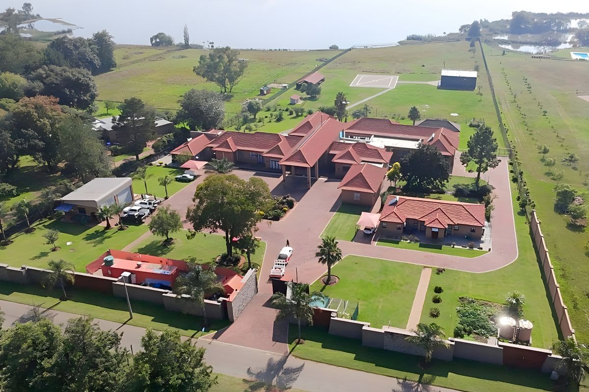 Aerial view of a large residential estate featuring multiple buildings, extensive paved driveways, landscaped grounds, and a private helicopter pad.