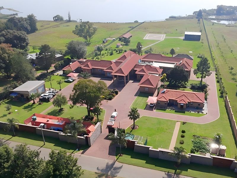 Aerial view of a large residential estate featuring multiple buildings, extensive paved driveways, landscaped grounds, and a private helicopter pad.