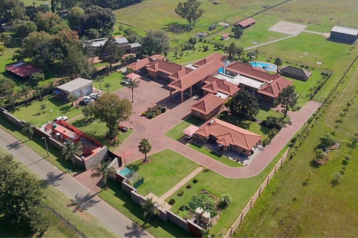Aerial view of a large residential estate featuring multiple buildings, a swimming pool, extensive paved driveways, landscaped gardens, and a private helicopter pad.