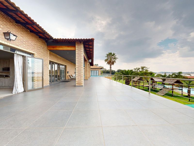 Spacious covered patio featuring tiled flooring, brick pillars, and a stainless steel balustrade, offering expansive views of the garden and pool area.