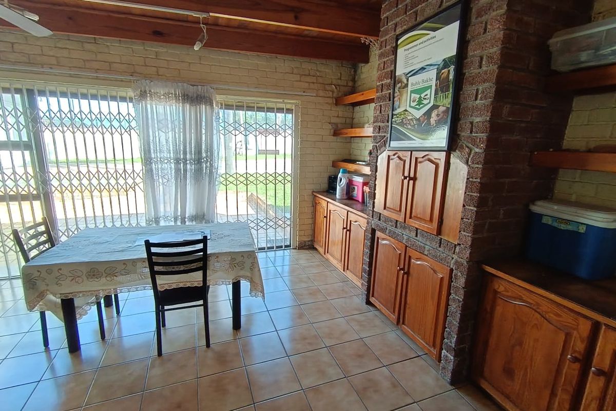 Living area featuring exposed timber beam ceilings, a brick fireplace, built-in wooden cabinetry, and tiled flooring with access to the garden through sliding doors.