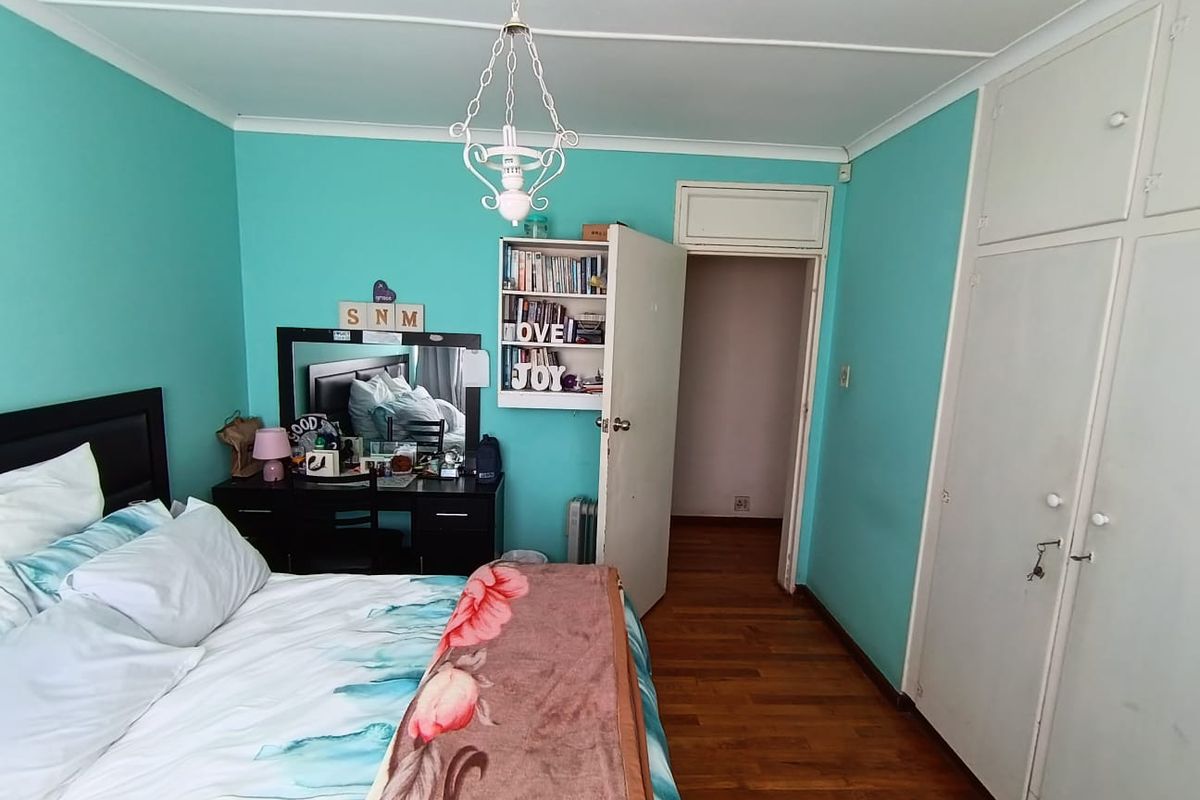 A bedroom featuring hardwood flooring, built-in wardrobe storage, and a decorative ceiling light fixture, finished with bright teal wall paint.