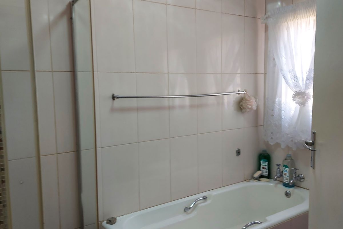 A functional bathroom featuring a bathtub, shower enclosure, and neutral wall tiling, offering a practical layout for daily use.