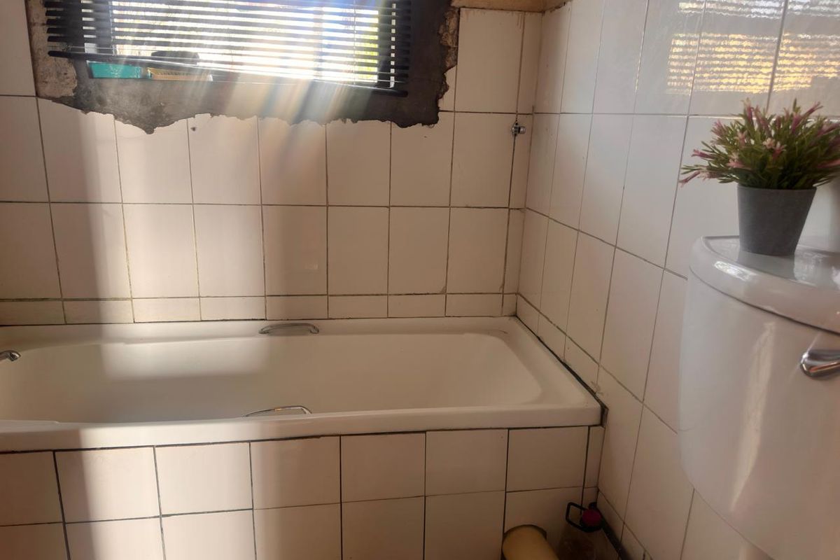 A bathroom featuring a bathtub and toilet, currently requiring significant repairs to the wall plaster and tiling around the window area.