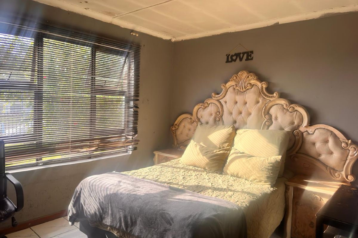 A bedroom featuring tiled flooring and venetian blinds, currently showing signs of wear on the ceiling and walls.