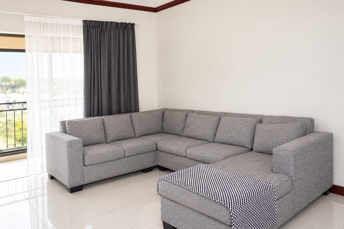 A bright living room featuring large format floor tiles, crown molding, and a sliding glass door providing access to a balcony with iron railings.