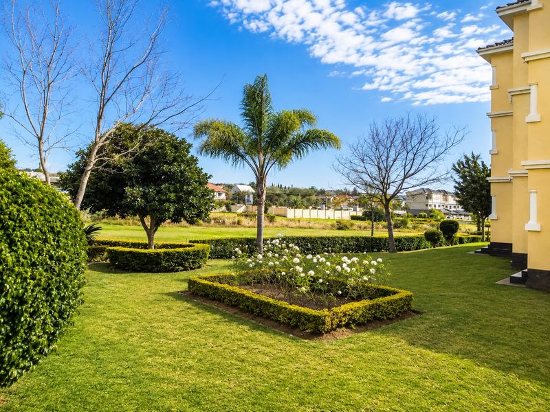 A well-maintained communal garden area featuring manicured lawns, structured hedges, and established trees adjacent to the apartment building.