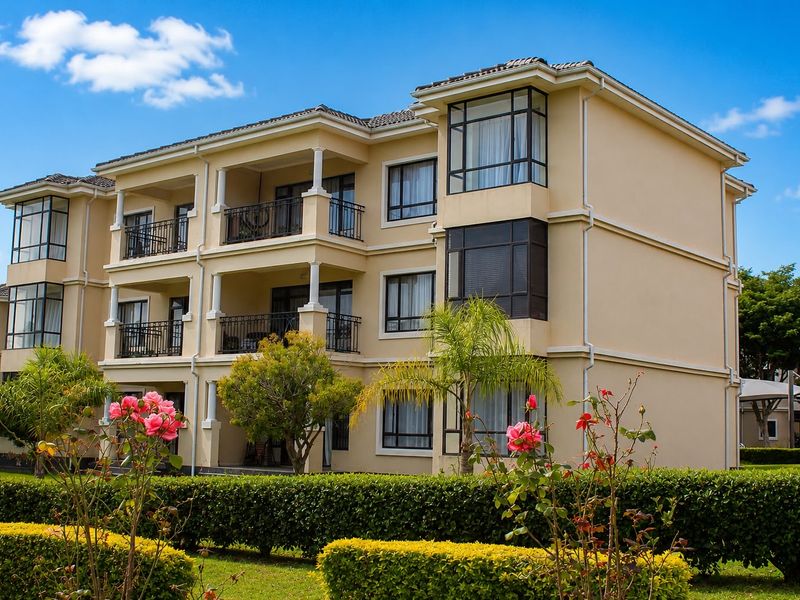 A well-maintained multi-story apartment building featuring private balconies, metal railings, and landscaped garden surrounds.
