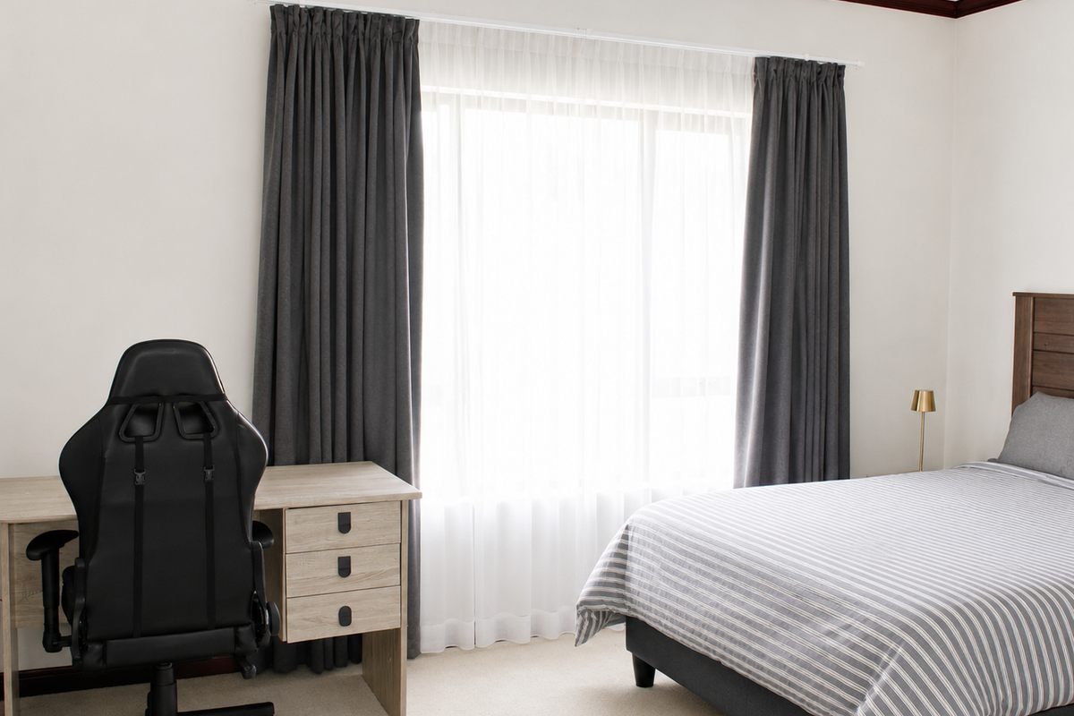 A well-maintained bedroom featuring neutral carpet flooring, timber crown molding, and large windows dressed with floor-to-ceiling curtains.
