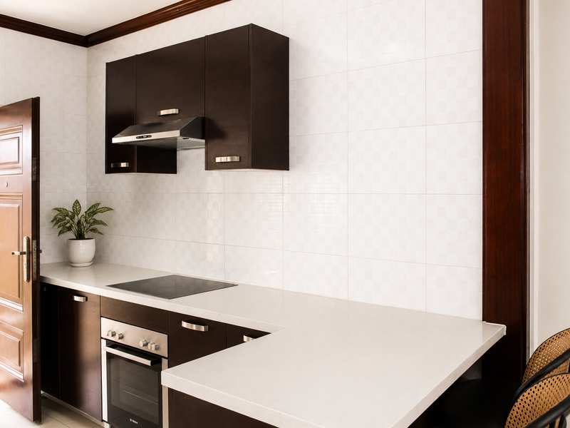 A modern kitchen featuring dark wood cabinetry, stone countertops, a built-in oven, and an electric cooktop with an integrated extractor fan.