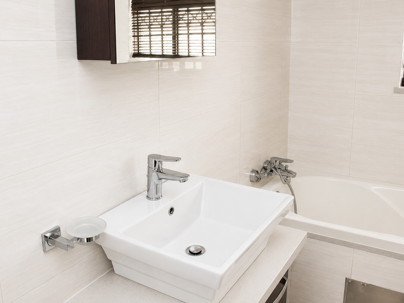 A clean, modern bathroom featuring a wall-mounted basin, chrome fixtures, and a built-in bathtub with neutral ceramic wall tiling.