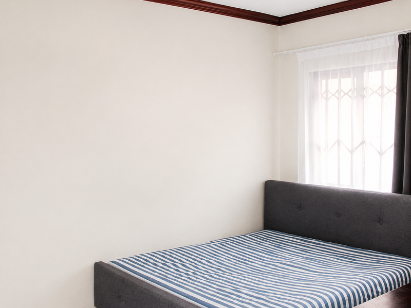 A simple bedroom featuring neutral walls, dark wood crown molding, and a window fitted with a security gate.