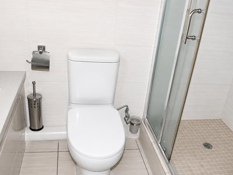 A clean, modern bathroom featuring a white toilet, a glass-enclosed shower, and neutral-toned wall and floor tiling.
