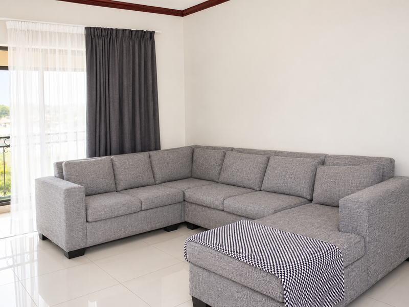 A bright living room featuring large format floor tiles, crown molding, and a sliding glass door providing access to a balcony with iron railings.