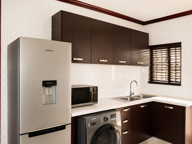 A well-maintained kitchen featuring dark wood cabinetry, a stainless steel double sink, tiled backsplash, and integrated laundry and microwave appliances.